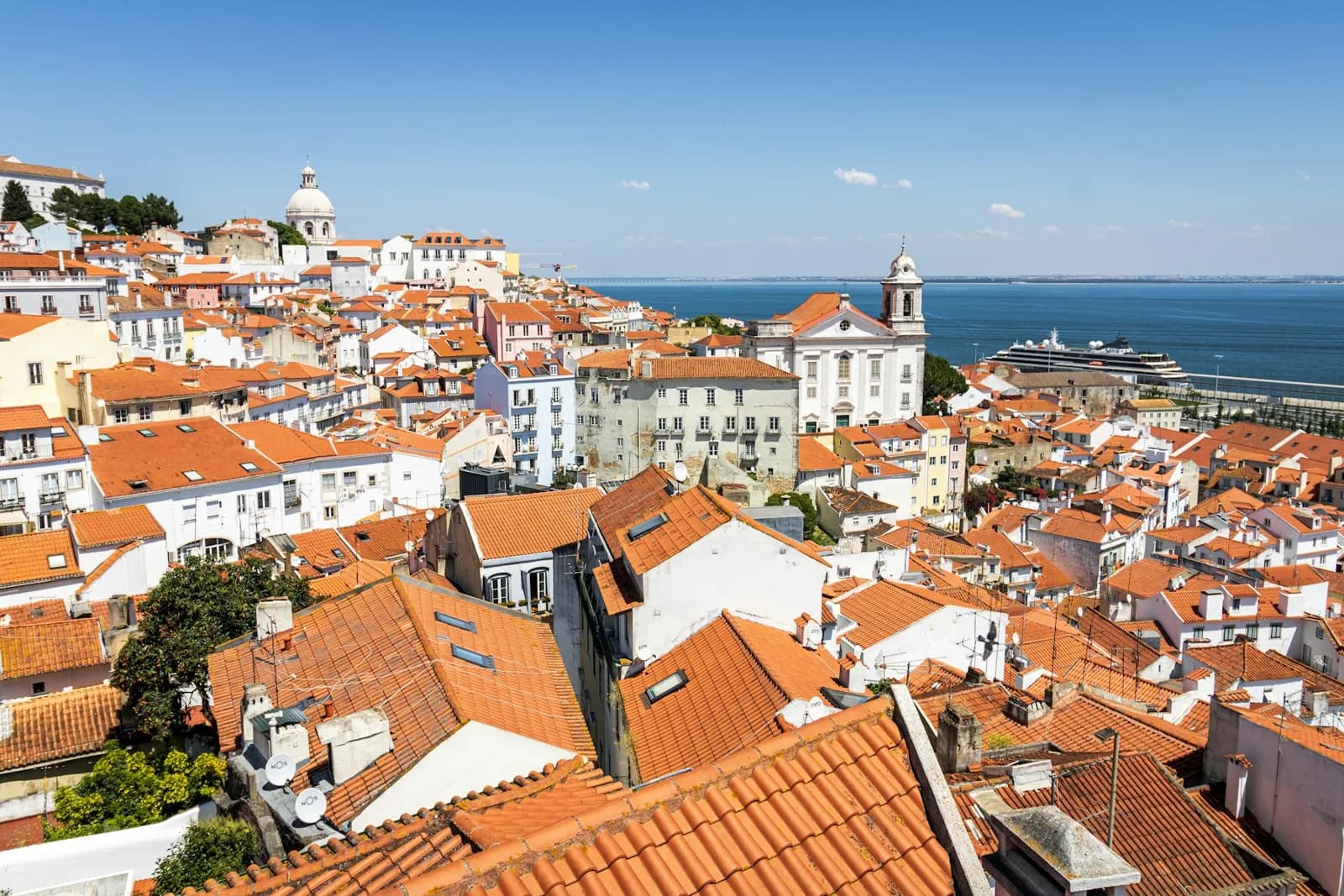 Terracotta rooftops and white churches in Alfama above Lisbon’s waterfront